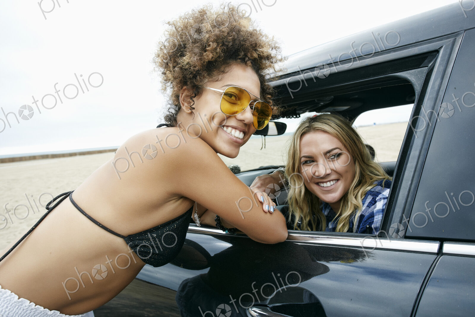 Young woman leaning against car door talking to a woman driver, friends
