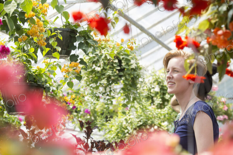 Young woman looking at colourful flowering plants in hanging baskets in a garden centre.