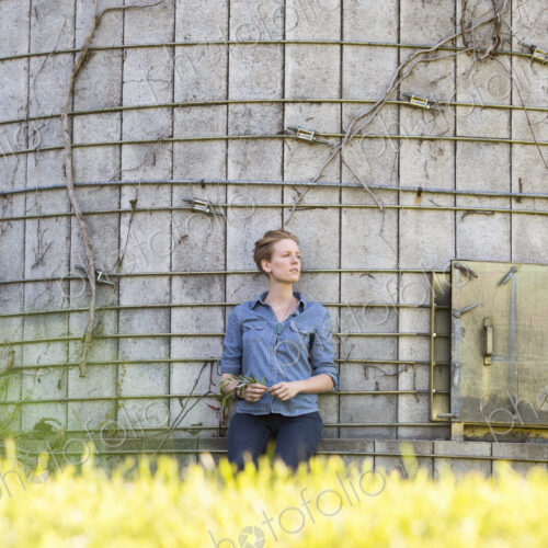 Young woman on a working farm, taking a break in the shade of a silo.