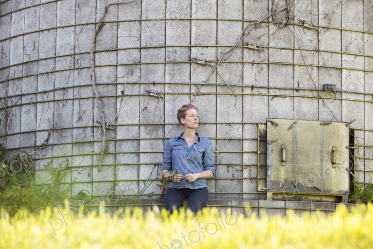 Young woman on a working farm, taking a break in the shade of a silo.