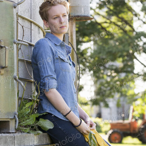 Young woman on a working farm, taking a break in the shade of a silo.