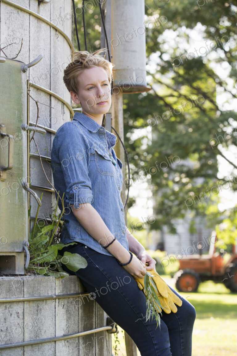 Young woman on a working farm, taking a break in the shade of a silo.