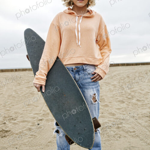 Young woman on sandy beach, holding skateboard, looking at camera. Young woman on sandy beach, holding skateboard, looking at camera.