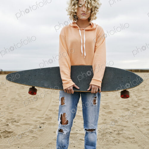 Young woman on sandy beach, holding skateboard, looking at camera. Young woman on sandy beach, holding skateboard, looking at camera.