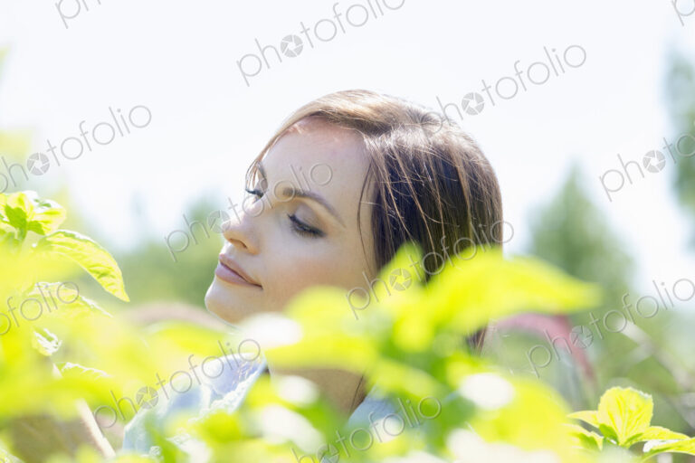 Young woman outdoors surrounded by green plants.