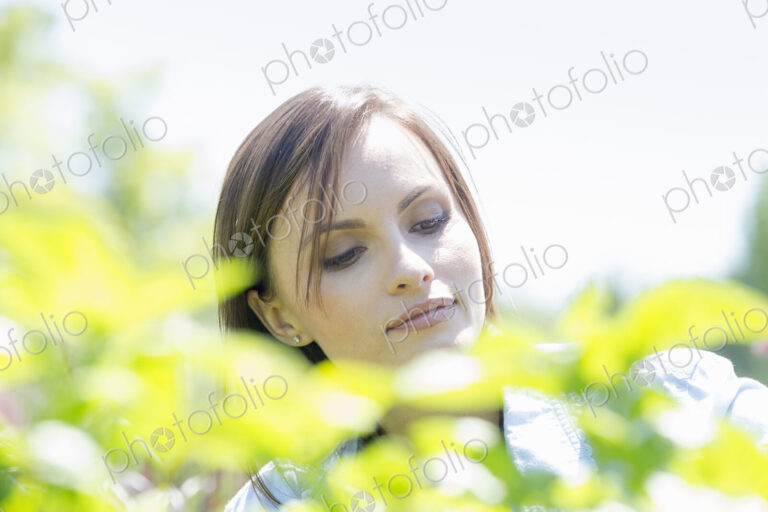 Young woman outdoors surrounded by green plants.