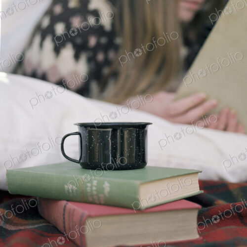 Young woman reading a book, a mug standing on two books.