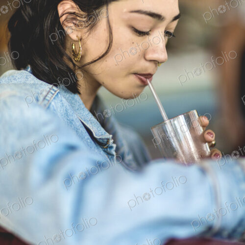 Young woman sitting at a bar counter, holding a glass, drinking with a straw. Young woman sitting at a bar counter, holding a glass, drinking with a straw.