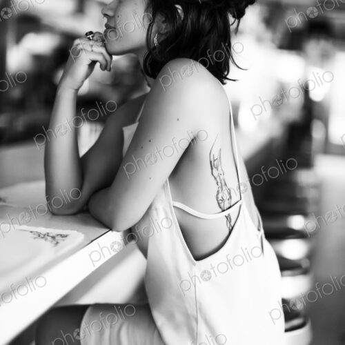 Young woman sitting on a stool at a bar counter in a diner, hand on chin.