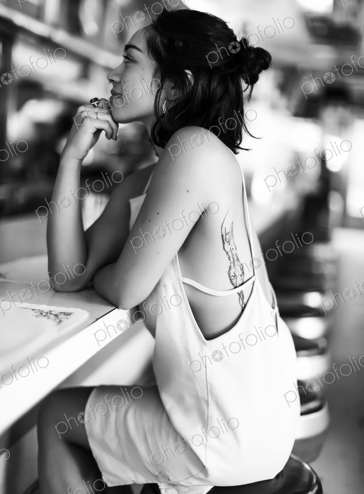 Young woman sitting on a stool at a bar counter in a diner, hand on chin.