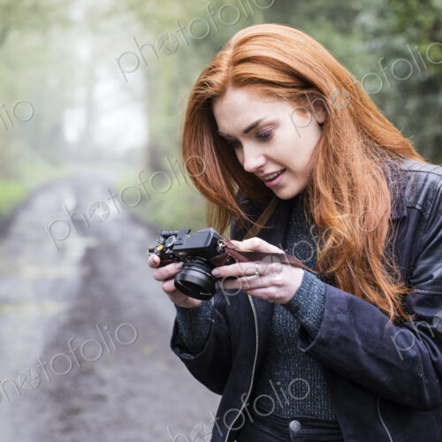 Young woman walking along forest path, with vintage camera.