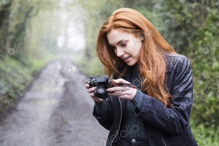 Young woman walking along forest path, with vintage camera.