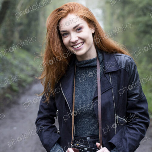 Young woman walking along forest path, with vintage camera.