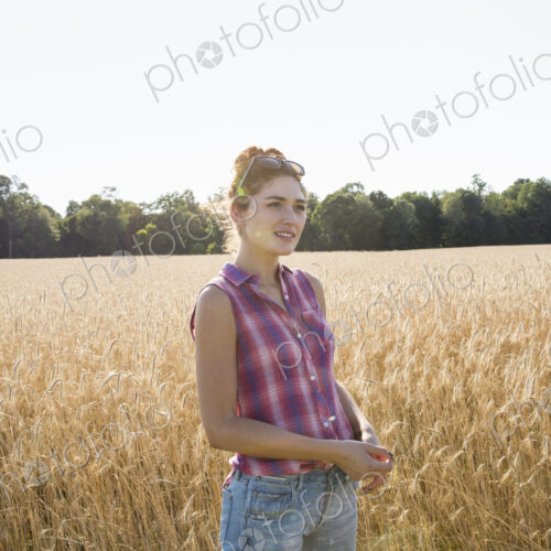 Young woman wearing a checkered shirt standing in a cornfield.
