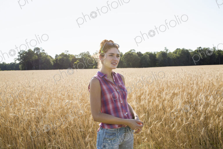 Young woman wearing a checkered shirt standing in a cornfield.