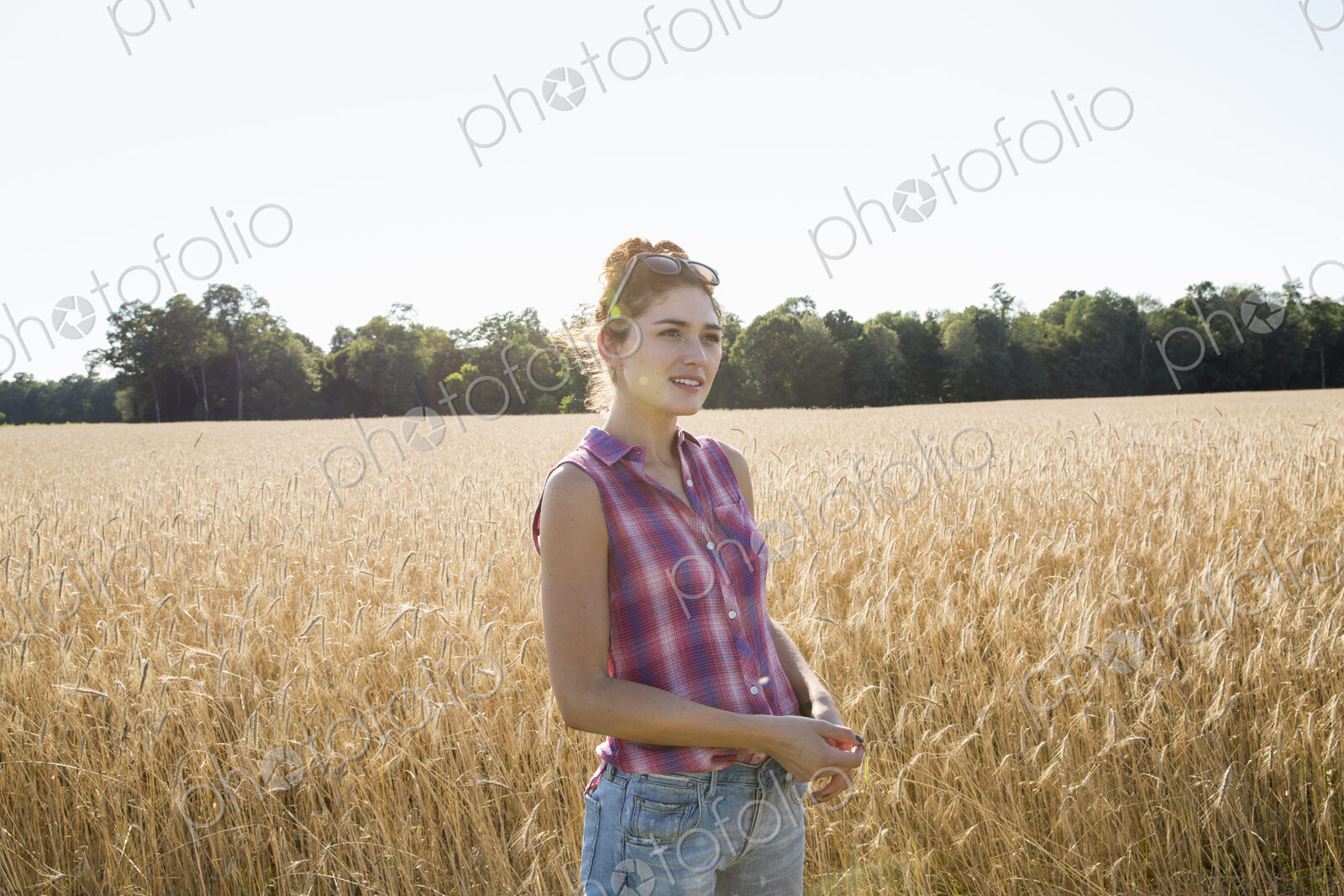 Young woman wearing a checkered shirt standing in a cornfield.