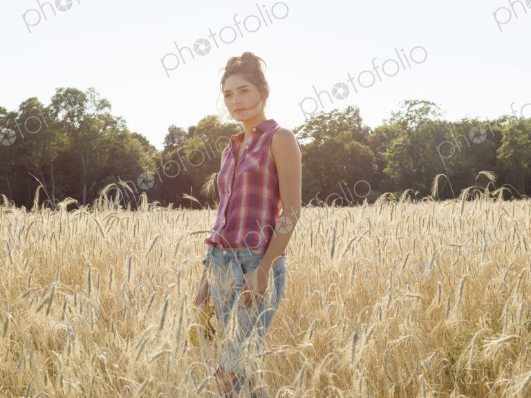 Young woman wearing a checkered shirt standing in a cornfield.