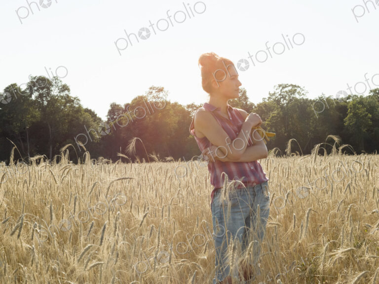 Young woman wearing a checkered shirt standing in a cornfield.