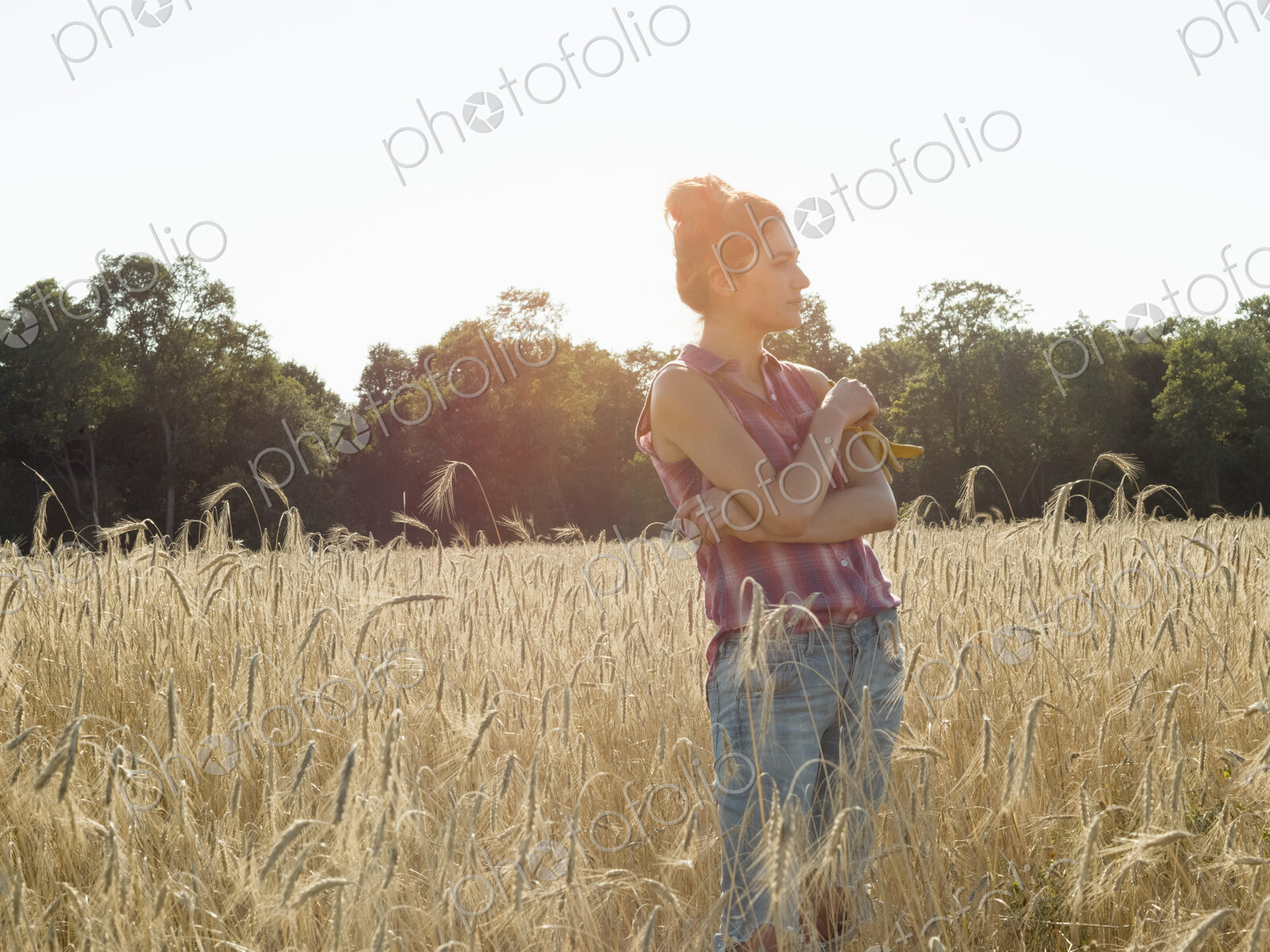 Young woman wearing a checkered shirt standing in a cornfield.