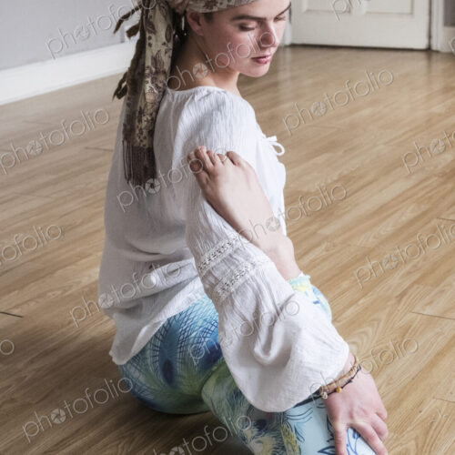 Young woman wearing headscarf and white blouse sitting on floor in yoga pose.