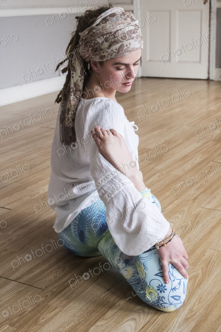 Young woman wearing headscarf and white blouse sitting on floor in yoga pose.