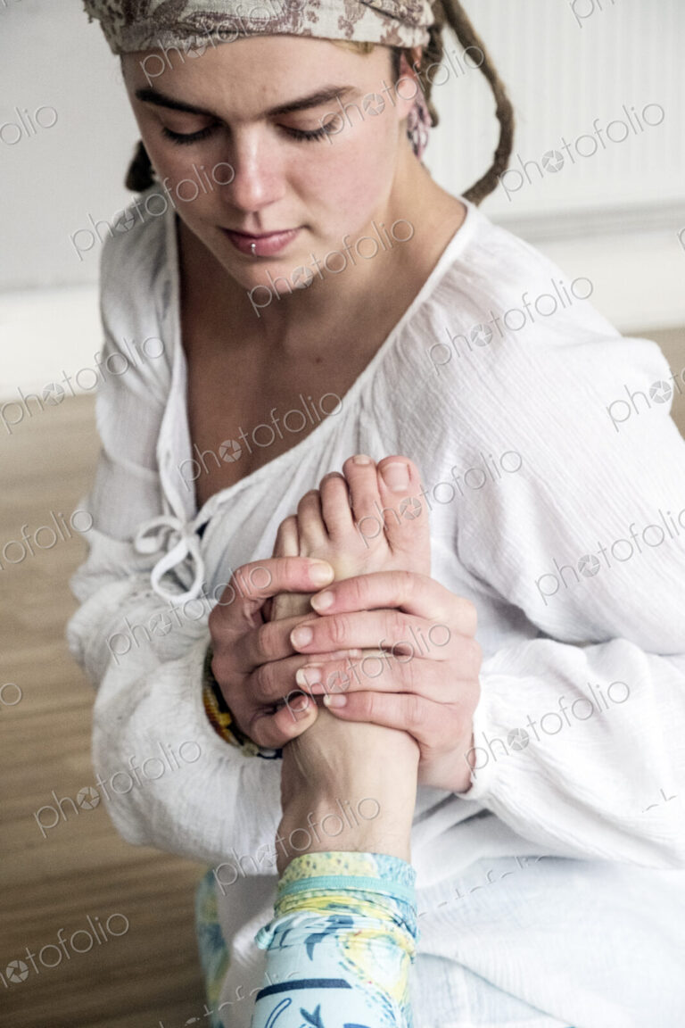 Young woman wearing headscarf and white blouse sitting on floor in yoga pose.