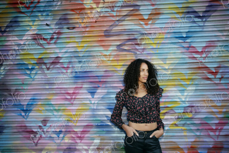 Young woman with black curly hair standing in front of shutter covered in colourful…
