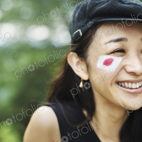 Young woman with black hair wearing flat cap, Japanese flag painted on her cheek.