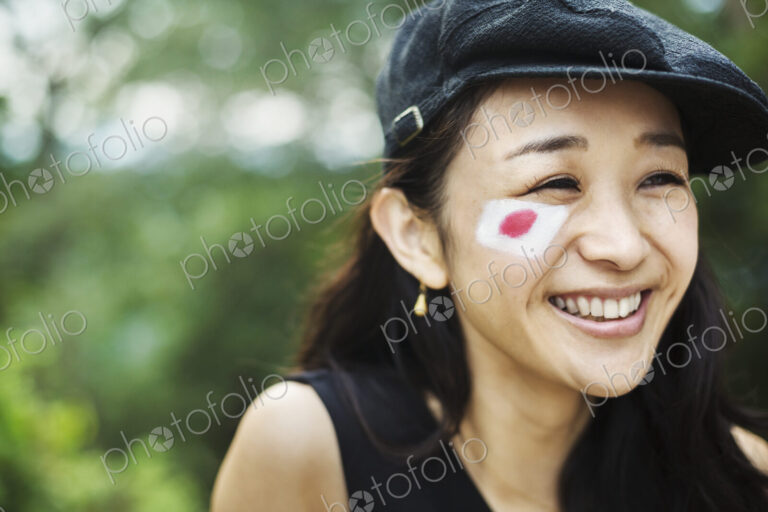 Young woman with black hair wearing flat cap, Japanese flag painted on her cheek.