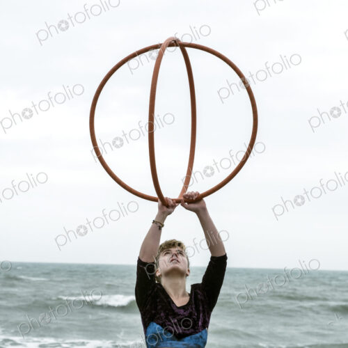 Young woman with brown hair and dreadlocks standing by the ocean, balancing two hula… Young woman with brown hair and dreadlocks standing by the ocean, balancing two hula…