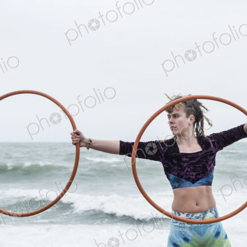 Young woman with brown hair and dreadlocks standing by the ocean, balancing two hula… Young woman with brown hair and dreadlocks standing by the ocean, balancing two hula…