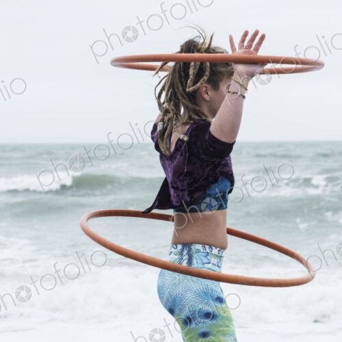 Young woman with brown hair and dreadlocks standing by the ocean, balancing two hula… Young woman with brown hair and dreadlocks standing by the ocean, balancing two hula…