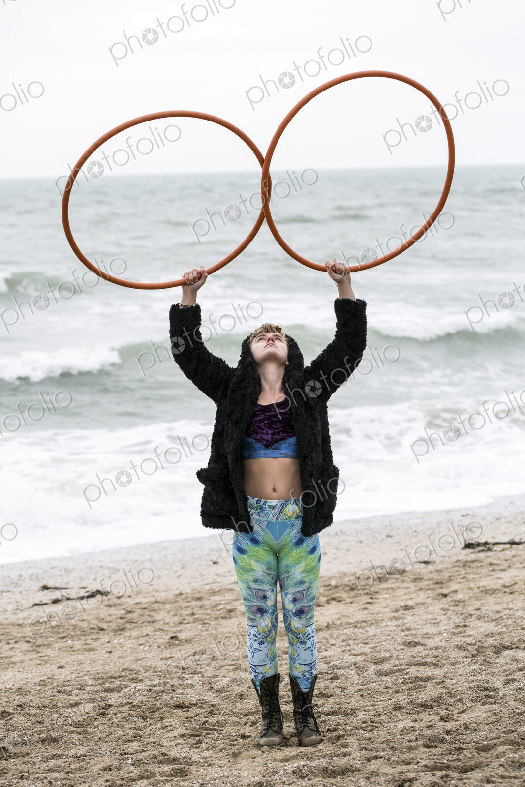 Young woman with brown hair and dreadlocks standing on a sandy beach by the ocean,…