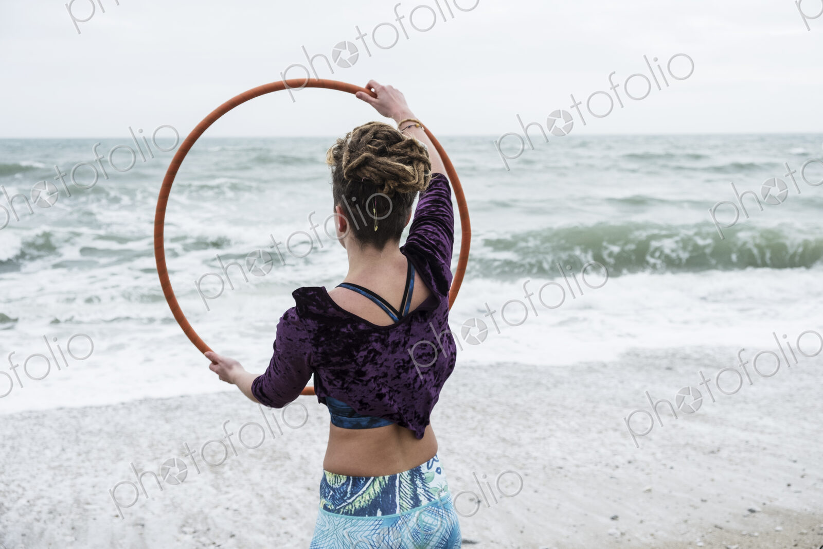 Young woman with brown hair and dreadlocks standing on a sandy beach by the ocean,…