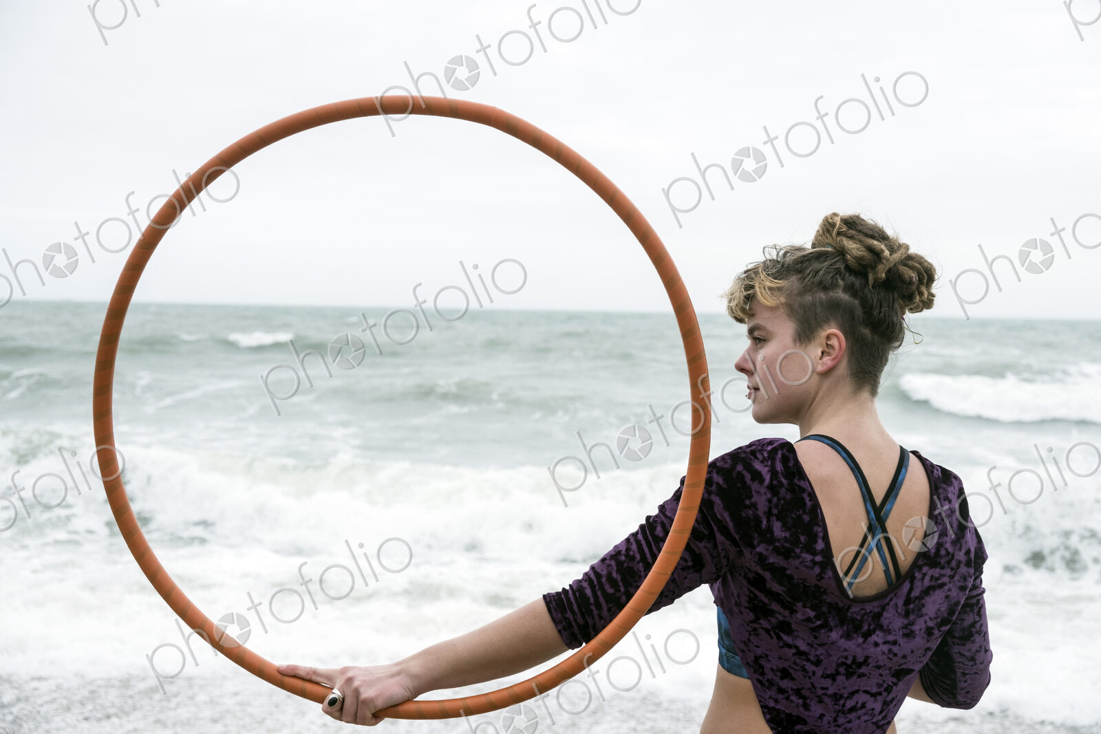 Young woman with brown hair and dreadlocks standing on a sandy beach by the ocean,…
