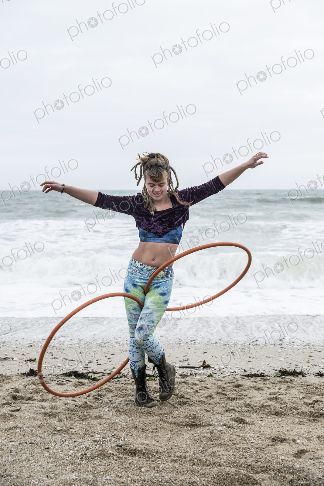 Young woman with brown hair and dreadlocks standing on a sandy beach by the ocean,…