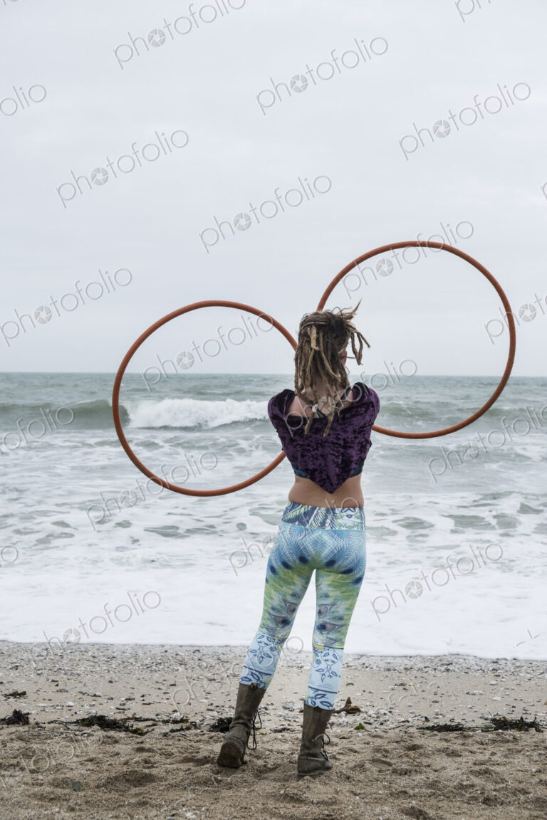 Young woman with brown hair and dreadlocks standing on a sandy beach by the ocean,…