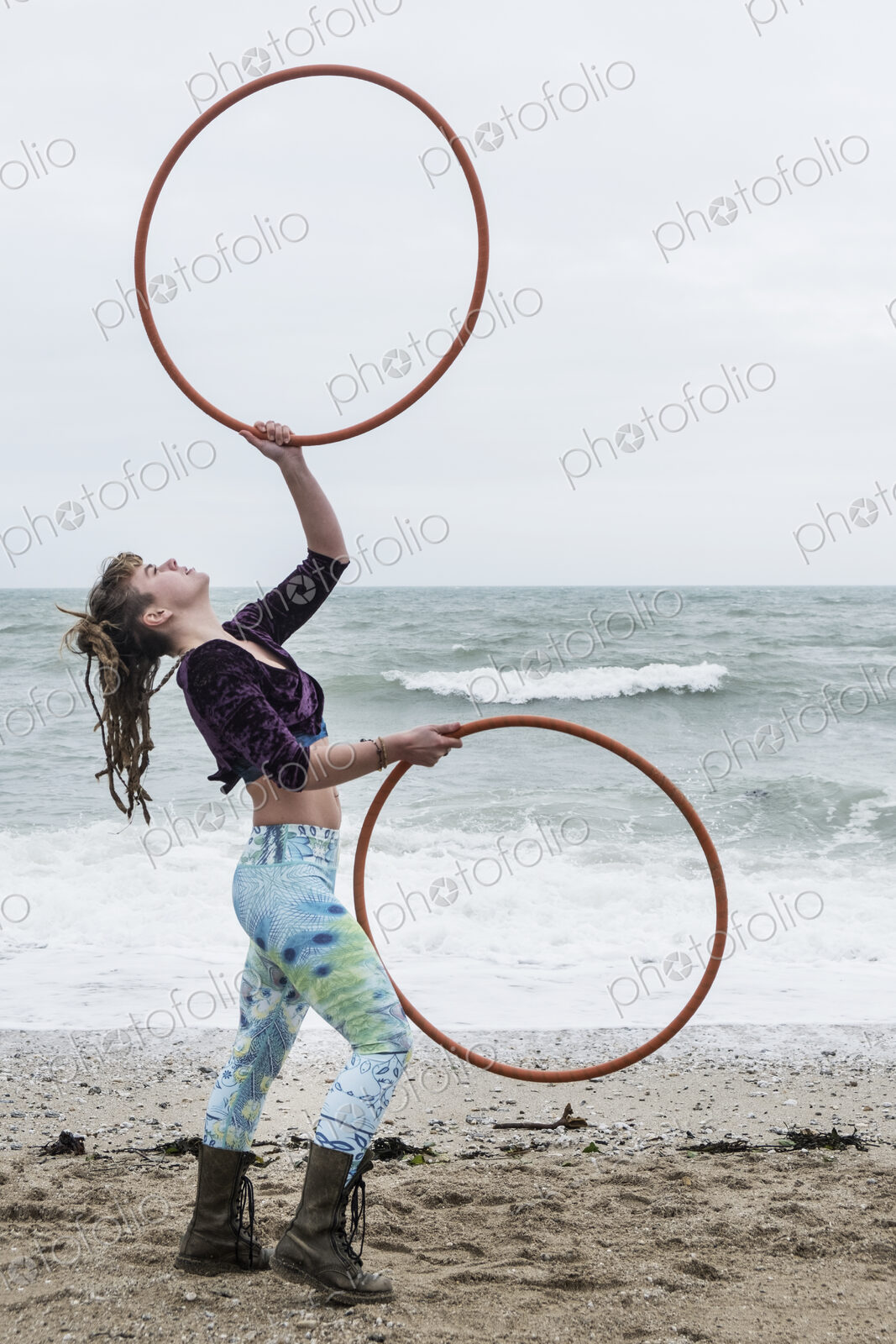 Young woman with brown hair and dreadlocks standing on a sandy beach by the ocean,…
