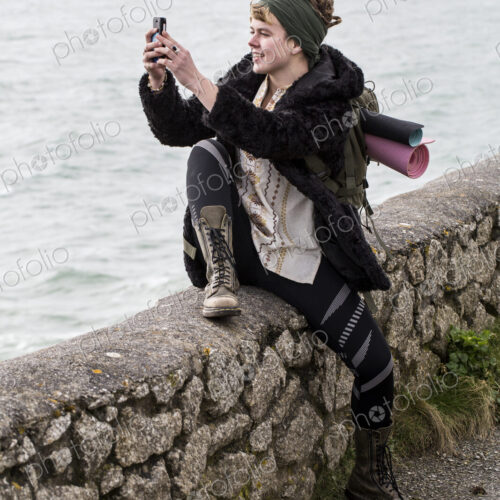 Young woman with brown hair and dreadlocks wearing headscarf sitting on dry-stone wall… Young woman with brown hair and dreadlocks wearing headscarf sitting on dry-stone wall…