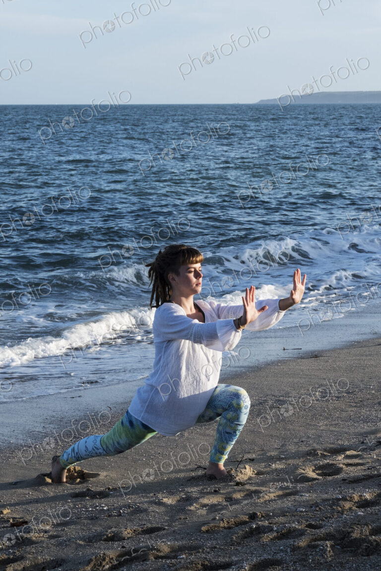 Young woman with brown hair wearing white blouse standing on a beach by the ocean,…