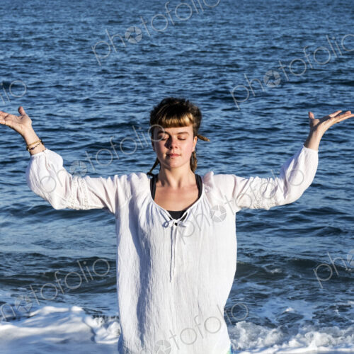 Young woman with brown hair wearing white blouse standing on a beach by the ocean,… Young woman with brown hair wearing white blouse standing on a beach by the ocean,…