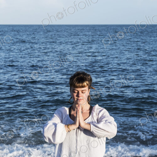 Young woman with brown hair wearing white blouse standing on a beach by the ocean,… Young woman with brown hair wearing white blouse standing on a beach by the ocean,…