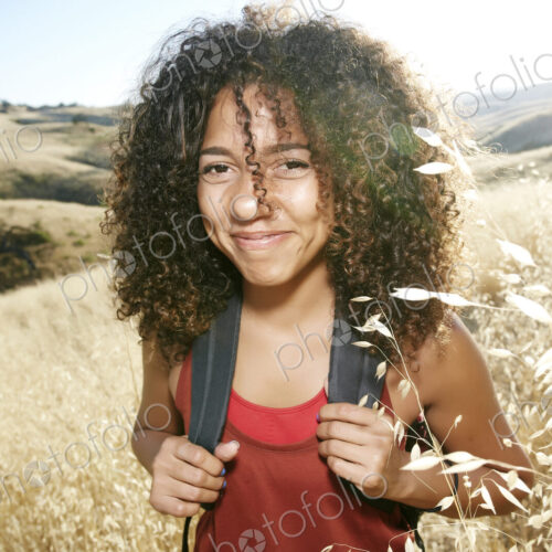 Young woman with curly brown hair hiking in urban park, smiling at camera. Young woman with curly brown hair hiking in urban park, smiling at camera.