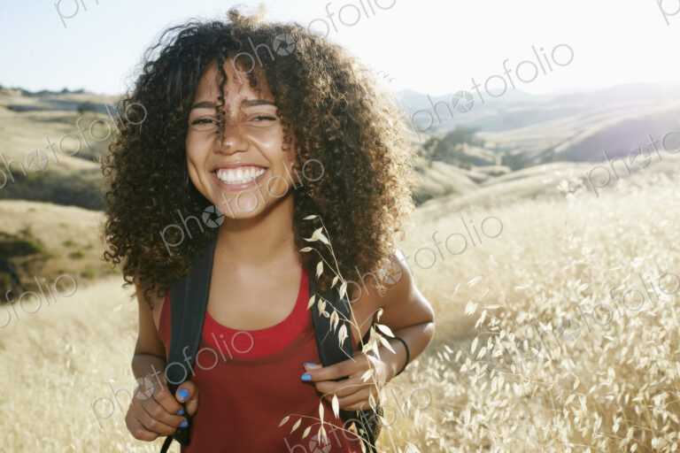 Young woman with curly brown hair hiking in urban park, smiling at camera.