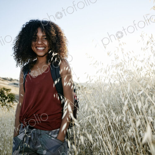 Young woman with curly brown hair hiking in urban park, smiling at camera. Young woman with curly brown hair hiking in urban park, smiling at camera.
