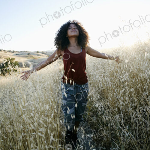 Young woman with curly brown hair hiking in urban park, standing in field, eyes closed. Young woman with curly brown hair hiking in urban park, standing in field, eyes closed.