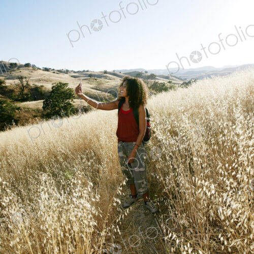 Young woman with curly brown hair hiking in urban park, taking picture with mobile phone. Young woman with curly brown hair hiking in urban park, taking picture with mobile phone.