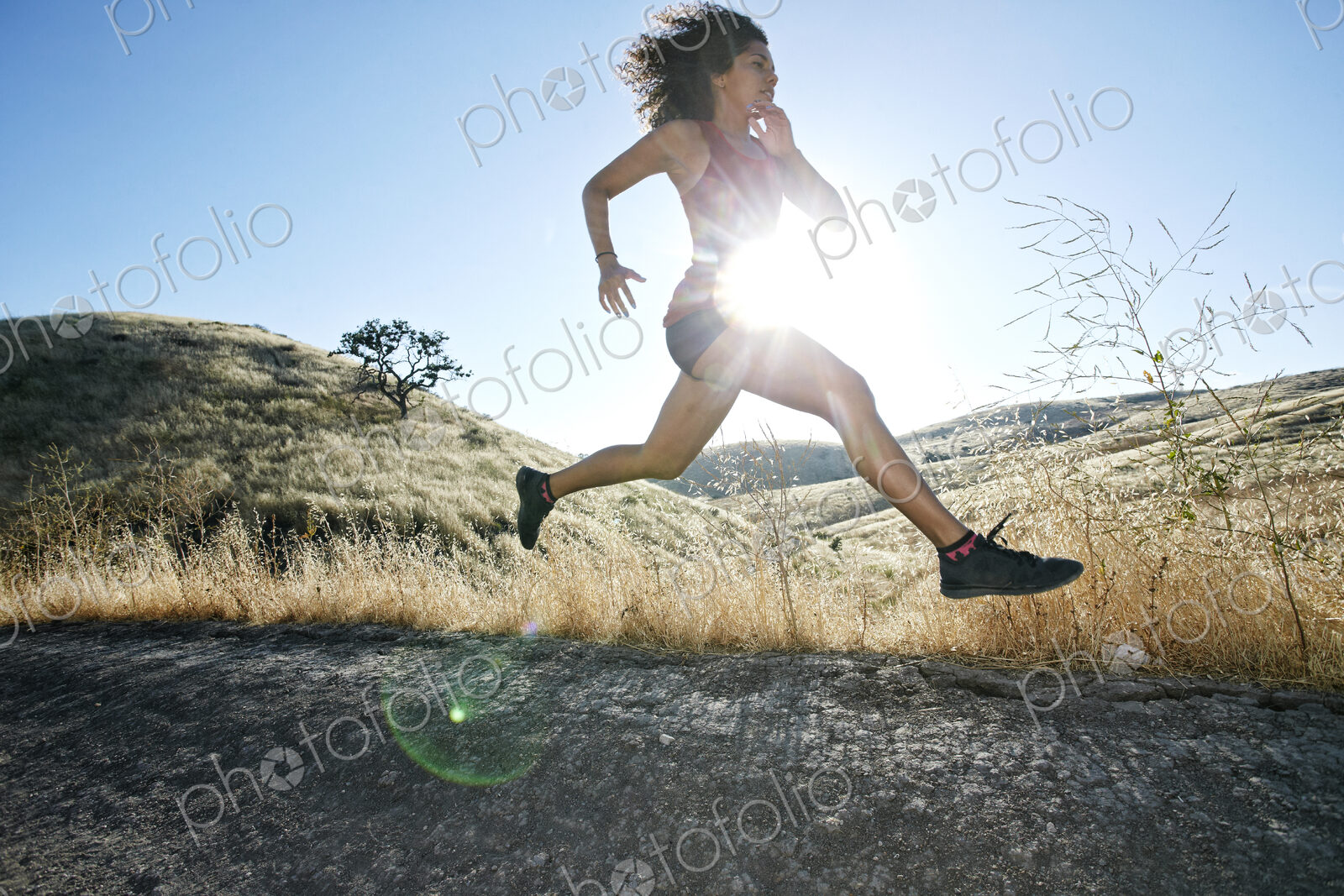 Young woman with curly brown hair running in urban park.