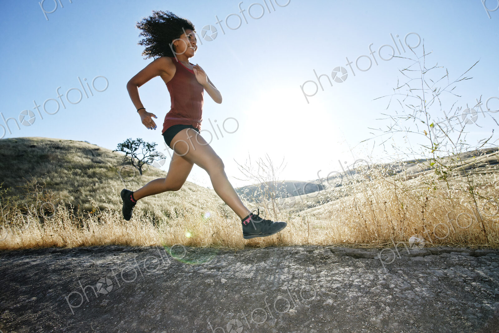 Young woman with curly brown hair running in urban park.