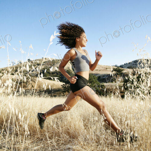 Young woman with curly brown hair running in urban park.